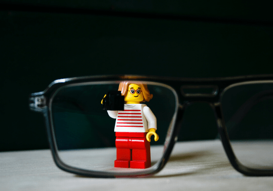 A lego woman standing behind the lens of a pair of glasses